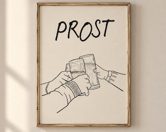 May include: A framed wall art print featuring a black line drawing of two hands clinking glasses together. Above the glasses, the word PROST is written in a bold, black, hand-lettered font. The background of the print is a solid, light cream color.