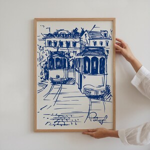May include: A blue and white sketch of two vintage trams in Lisbon, Portugal. The trams are drawn in a simple, stylized way, with the buildings in the background also sketched in blue.