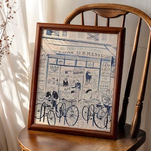 May include: A framed print featuring a blue and white ink illustration of a Parisian cafe scene titled AU PETIT FER A CHEVAL CAFE BAR DU BRESIL. The artwork depicts people sitting at tables with bicycles parked in front of the storefront.