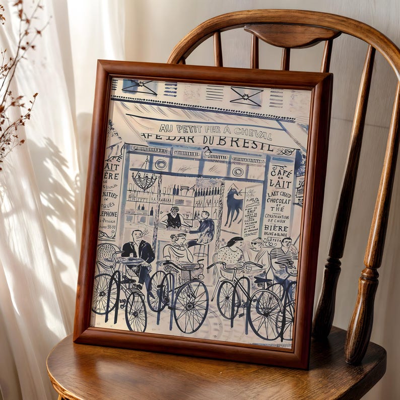 May include: A framed print featuring a blue and white ink illustration of a Parisian cafe scene titled AU PETIT FER A CHEVAL CAFE BAR DU BRESIL. The artwork depicts people sitting at tables with bicycles parked in front of the storefront.