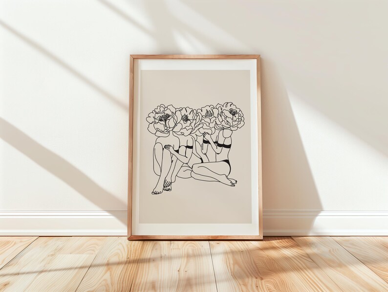 Puede incluir: Una impresi&oacute;n art&iacute;stica enmarcada con un dibujo lineal minimalista de tres figuras con cabezas florales. La obra de arte es en blanco y negro, sobre un fondo beige, y enmarcada en madera clara. La impresi&oacute;n se exhibe sobre un suelo de madera.