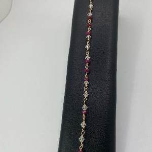 May include: A gold chain bracelet with alternating clear and burgundy beads.