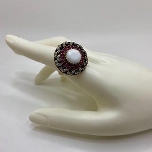 May include: A silver ring with a white stone surrounded by a circle of pink and clear stones.