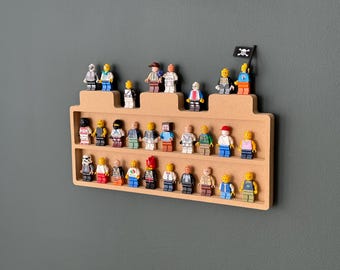 Może przedstawiać: Drewniana półka z dwoma półkami do przechowywania figurek Lego. Półka ma kształt zamku i ma na górze czarną flagę piracką. Na półkach znajduje się 25 figurek, w tym różne postacie i kolory.