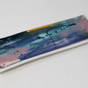 May include: A rectangular ceramic serving tray with an abstract design featuring shades of blue, green, pink, and yellow. The tray has a white background and a glossy finish.