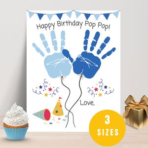 May include: A white birthday card with blue handprints forming balloons, the text "Happy Birthday Pop Pop!" and "Love," is displayed. A cupcake and a gold gift box are on the table. A yellow circle indicates 3 sizes.