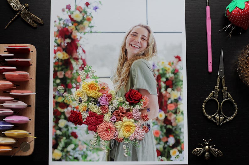 K&ouml;nnte beinhalten: Eine Frau mit langen blonden Haaren h&auml;lt einen Strau&szlig; bunter Seidenblumen. Die Blumen sind in verschiedenen Formen und Gr&ouml;&szlig;en angeordnet, darunter Rosen, G&auml;nsebl&uuml;mchen und Lilien. Die Frau tr&auml;gt ein hellgr&uuml;nes Kleid und l&auml;chelt.