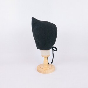 May include: A black knitted baby bonnet with a pointed top and a tie at the back.
