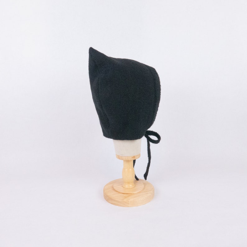 May include: A black knitted baby bonnet with a pointed top and a tie at the back.