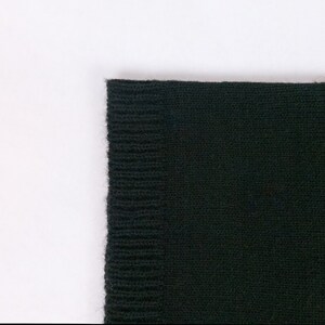 May include: Close-up of the edge of a black knitted scarf. The knit is a fine gauge and the fabric is soft.