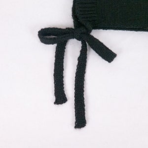 May include: Black knitted hat with two long ties that can be tied under the chin.