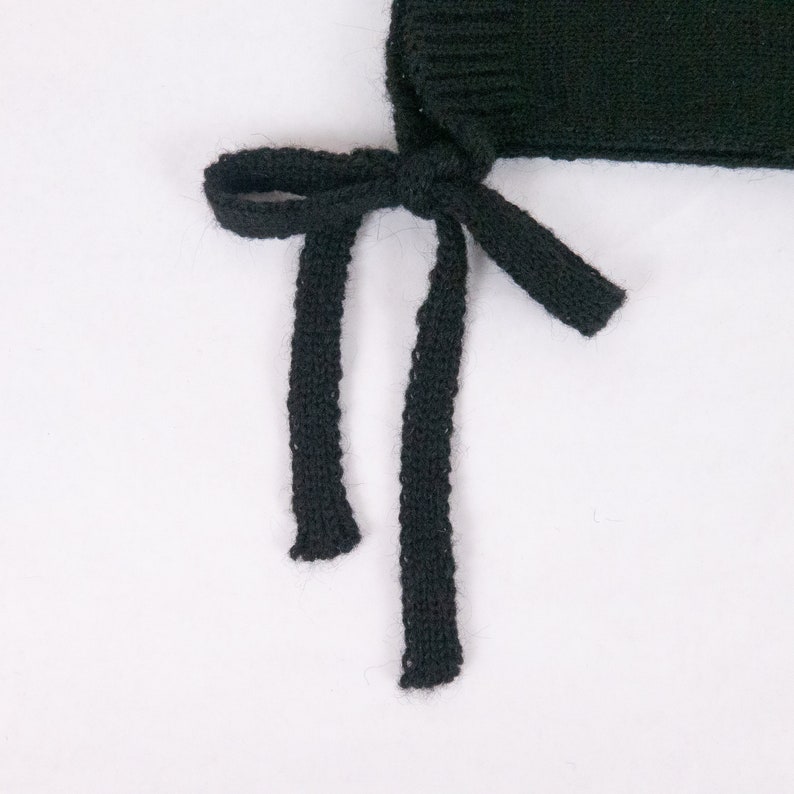 May include: Black knitted hat with two long ties that can be tied under the chin.