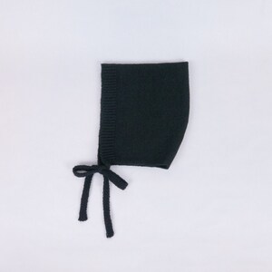 May include: A black knitted baby bonnet with ties. The bonnet is made of a soft, stretchy fabric and has a simple design.