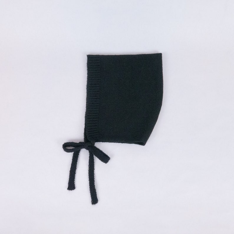 May include: A black knitted baby bonnet with ties. The bonnet is made of a soft, stretchy fabric and has a simple design.