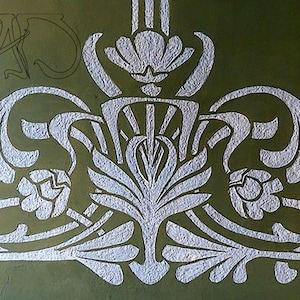 May include: A white stencil design of a stylized floral motif on a green background. The design features a central flower with three leaves on each side.