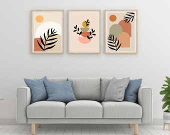 May include: Three framed abstract art prints with a minimalist design featuring geometric shapes, leaves, and circles in shades of brown, orange, green, and yellow. The prints are hung on a white wall above a light gray sofa.