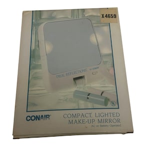 May include: A Conair compact, lighted make-up mirror with the text "TRUE REFLECTIONS" and "COMPACT, LIGHTED MAKE-UP MIRROR". The mirror is white with a rectangular shape and a light blue mirror surface. The packaging is white and blue.