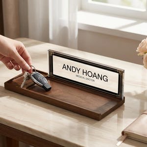 May include: A wooden desk tidy with a nameplate reading "ANDY HOANG, MEDICAL DOCTOR." The tidy holds keys and a car key fob. A bouquet of roses sits in a vase nearby. The desk is made of wood.