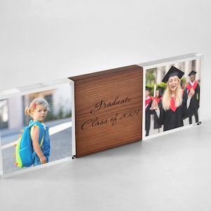 May include: A clear acrylic photo block with a wooden centre section. The block displays two photos, one of a young girl with a backpack and another of a graduate in a cap and gown. The wooden section has the text "Graduate Class of 2024".