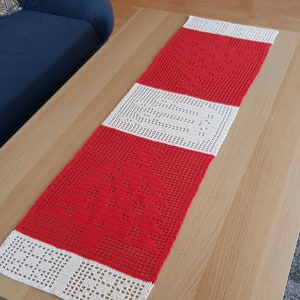 Może przedstawiać: Biało-czerwony szydełkowy bieżnik stołowy z geometrycznym wzorem. Bieżnik leży na drewnianym stole.