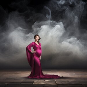 May include: A pregnant person in a long, flowing, magenta gown stands in a smoky, dark studio setting. The person is looking directly at the camera with a neutral expression.