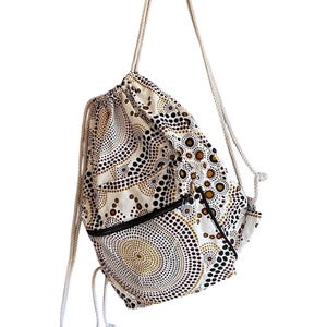 Può includere: Uno zaino bianco con coulisse e un design a motivi marroni, neri e dorati. Lo zaino ha due tasche con cerniera sul davanti.