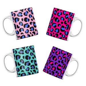 May include: Four white ceramic mugs with leopard print designs. The mugs have pink, turquoise, purple, and fuchsia backgrounds with black and blue spots. Each mug has a white handle.