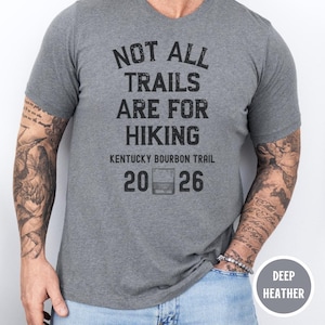 May include: Deep heather gray V-neck t-shirt with the text "NOT ALL TRAILS ARE FOR HIKING". The shirt also features "Kentucky Bourbon Trail" and the numbers "20 26" with a whiskey glass graphic.