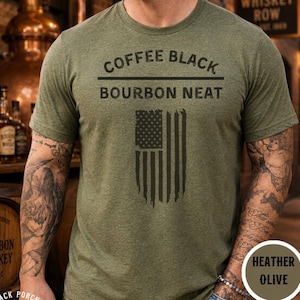Op de afbeelding: Een heather olijfgroen t-shirt met korte mouwen en de zwarte tekst COFFEE BLACK BOURBON NEAT boven een afbeelding van een verticale Amerikaanse vlag. Het ontwerp is gecentreerd op de borst van het shirt, dat een ronde halslijn heeft.