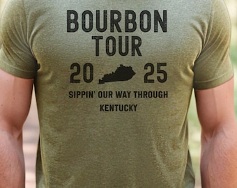 May include: Green t-shirt with black text that reads "Bourbon Tour 20 25 Sippin' Our Way Through Kentucky". The shirt features a black silhouette of the state of Kentucky.