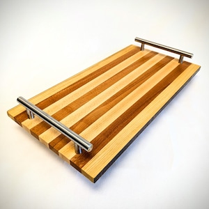 May include: A rectangular wooden serving tray with a striped pattern of light and dark wood. The tray has two silver metal handles.
