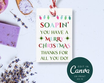 Op de afbeelding: Een wit cadeau-etiket met een rood, roze, groen en blauw ontwerp. Het etiket zegt "SOAPIN' YOU HAVE A MERRY CHRISTMAS THANKS FOR ALL YOU DO!" en heeft een touwtje eraan bevestigd. Het etiket is op een witte achtergrond.