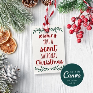 May include: White gift tag with green foliage and red text that reads "Wishing you a scent-sational Christmas". The tag is tied with a red and white twine and is surrounded by pine branches, pine cones, and red berries.