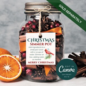 Puede incluir: Un tarro de vidrio lleno de palitos de canela, an&iacute;s estrellado, ar&aacute;ndanos y c&aacute;scara de naranja. Una etiqueta blanca con el texto "Christmas Simmer Pot" e instrucciones de uso est&aacute; unida al tarro. La etiqueta tambi&eacute;n incluye una ilustraci&oacute;n de un cardenal rojo y el texto "Merry Christmas".