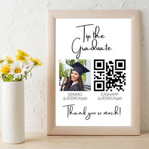 May include: A white sign with black text that says "Tip the Graduate". There is a photo of a graduate in a cap and gown holding a diploma. Below the photo are the words "Venmo: @Jessica340" and "Cashapp: @Jessica340". There is a QR code to the right of the photo. The sign also says "Thank you so much!"