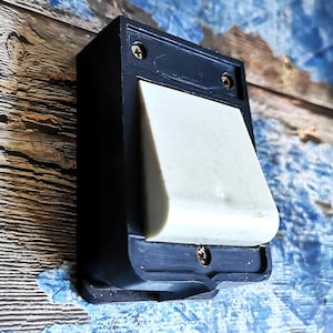 Könnte beinhalten: Ein schwarzer Lichtschalter mit einem weißen Kippschalter. Der Schalter ist an einer Holzwand mit blauer Farbe montiert.