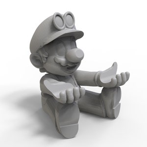 Può includere: Una statuetta grigia di un personaggio che indossa un berretto con gli occhiali, seduto con le gambe incrociate e le mani allargate.