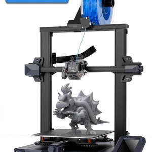 May include: A black 3D printer with a blue filament spool, a grey 3D printed model, and a touchscreen display. The printer has a black frame and a blue filament spool. The 3D printed model is a grey figure of a character from a video game. The touchscreen display is on the front of the printer.
