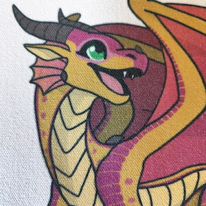 Puede incluir: Primer plano de un drag&oacute;n de dibujos animados con cuerpo amarillo, detalles rosas y ala roja. El drag&oacute;n tiene ojos verdes, cuernos negros y expresi&oacute;n sonriente. La imagen est&aacute; sobre un fondo blanco.