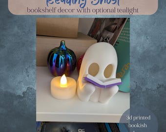 May include: A white 3D-printed ghost figurine reading a purple book, with a battery-operated tealight candle and a decorative iridescent pumpkin. The text reads "Reading Ghost bookshelf decor with optional tealight."