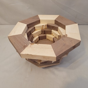 May include: A wooden bowl with a geometric octagonal shape. The bowl is made of alternating light and dark wood, creating a checkered pattern. The bowl is stacked in layers, creating a unique and intricate design.