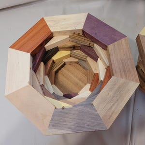 May include: A wooden bowl with a geometric design, made from different types of wood, including light brown, dark brown, purple, and yellow.