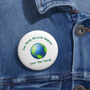May include: A white button with a green and blue globe graphic and the text "Eat Sleep Recycle Repeat Save The Earth".