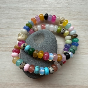 Puede incluir: Dos pulseras hechas de cuentas multicolores, lisas, redondas y con forma de disco. Las cuentas presentan una variedad de colores que incluyen rosa, azul, amarillo, verde, negro, blanco y tonos translúcidos, con algunas cuentas que muestran patrones moteados.