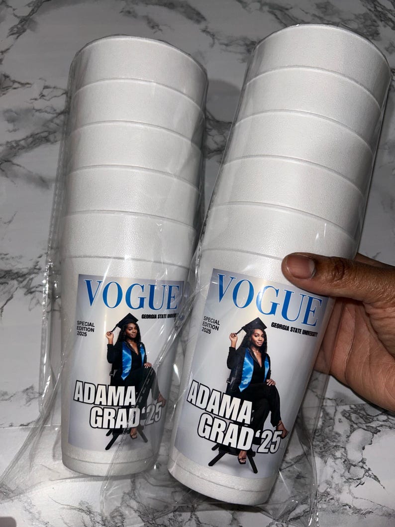 May include: Two stacks of white foam cups, each with a custom label. The label features the Vogue logo, a photo of a graduate, and the text "ADAMA GRAD '25". The cups are packaged in clear plastic.