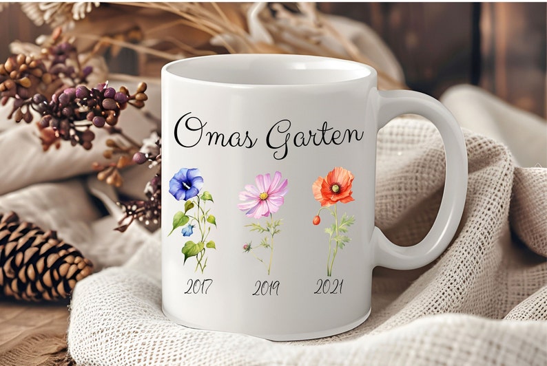 May include: White ceramic mug with a black inscription "Omas Garten" and three watercolor flowers with the years 2017, 2019, and 2021 printed below them.