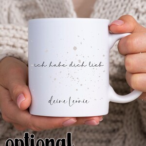 May include: White ceramic mug with a speckled design. The mug has black text that reads "ich habe dich lieb deine Leonie".
