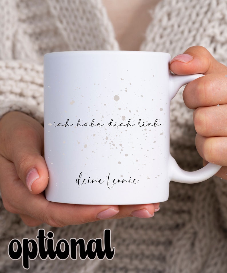 May include: White ceramic mug with a speckled design. The mug has black text that reads "ich habe dich lieb deine Leonie".