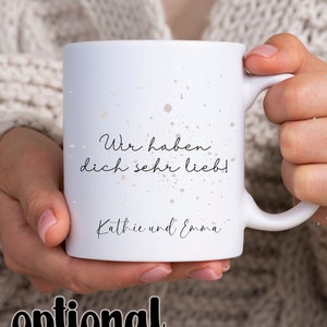 May include: White ceramic mug with a black and white splatter design. The mug has the text "Wir haben dich sehr lieb!" and "Kathie und Emma" printed on it.