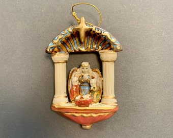 Porcelain Christmas ornament. A nativity scene is in the middle with two pillars on either side and a gold canopy overhead.